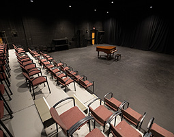Studio theatre with a baby grand piano and a four rows of empty seats.