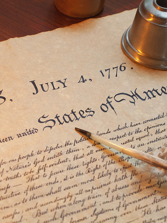 A quill pen, vintage-style spectacles and a vintage-style candlestick on the Declaration of Independence.