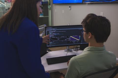 An instructor pointing at data visualizations and code on a computer monitor while working with a student.