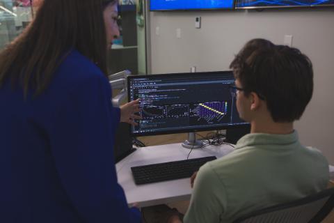 An instructor pointing at data visualizations and code on a computer monitor while working with a student.