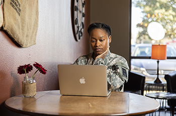 U.S. service member in uniform looking at laptop while sitting at a table in a cafe.