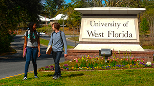 Two students walking by the University of West Florida campus entrance sign.