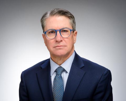 A professor in a dark blue suit with a blue tie, wearing blue glasses.