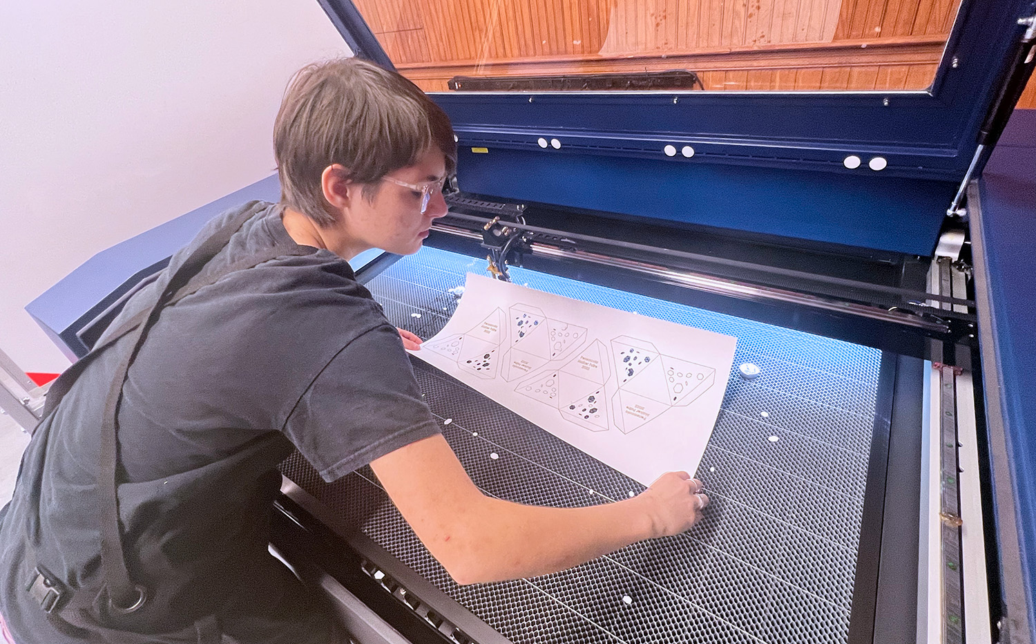 A student is laser cutting paper using machinery.
