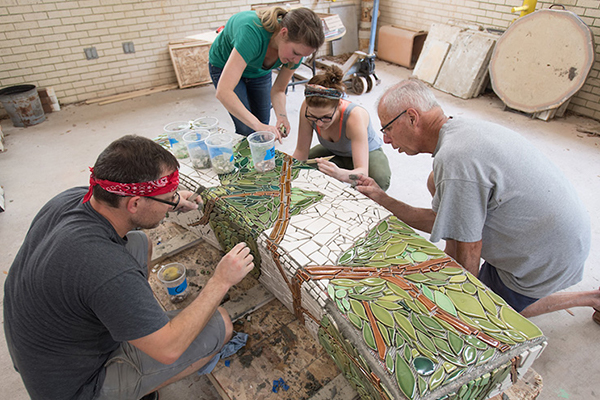 students collaborate on a mosaic bench