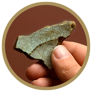 A hand holds a broken pottery fragment with a white glaze on it