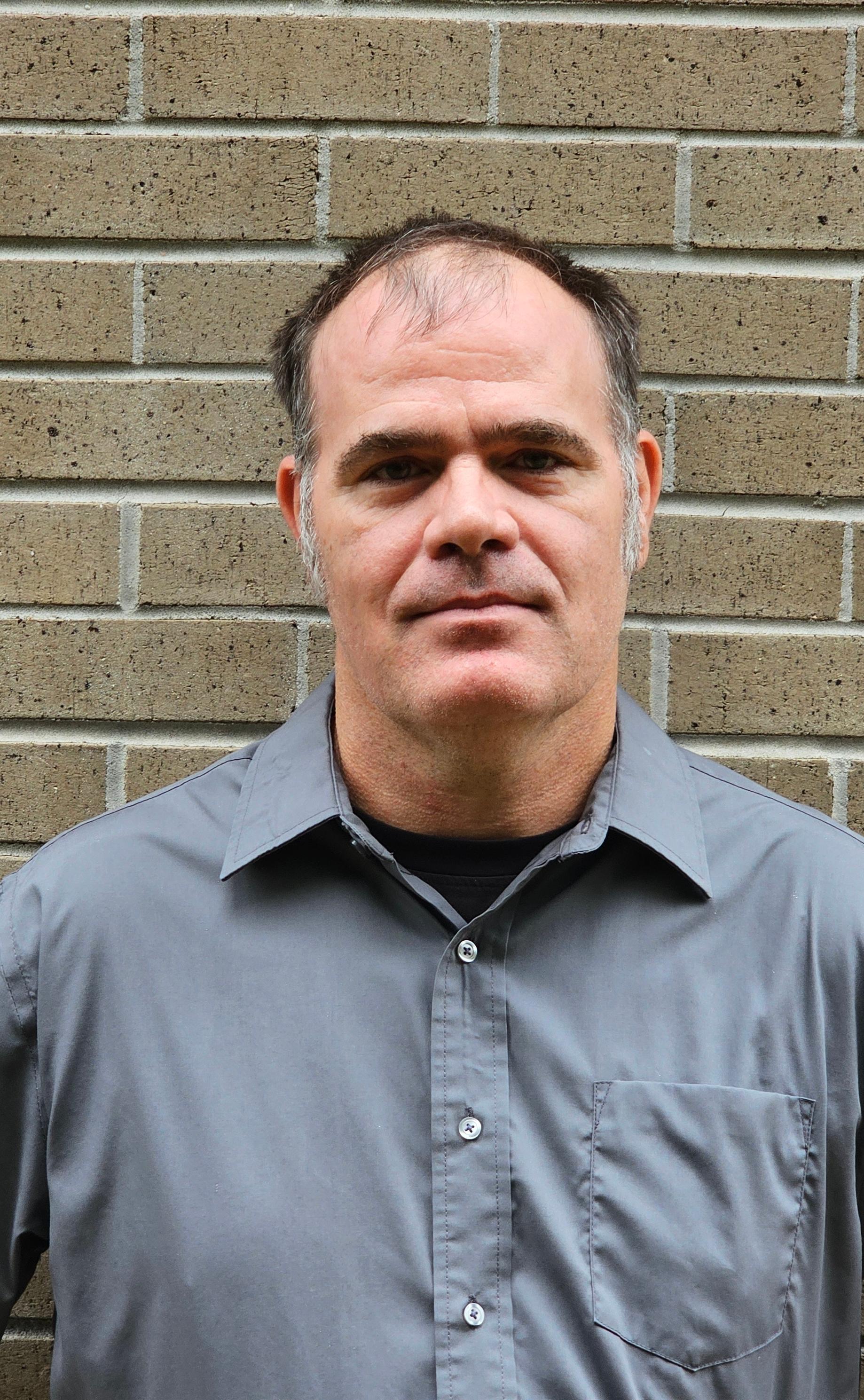 Rockie Jarvis outdoor headshot against a brick wall.