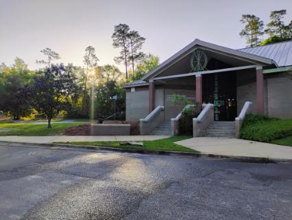 The front of the Margaret Jane Smith Archaeology Institute Building. Two sidewalks and sets of stairs lead to a entry with a peaked roof featuring a turtle medallion the sun is rising in the background