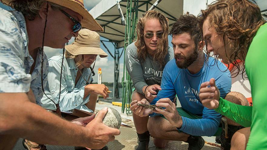 Students and Faculty examine a stone cannon ball and other objects from the Luna shipwrecks