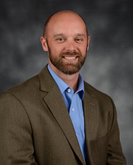 Matthew Crow indoor headshot in professional attire against a gray background.