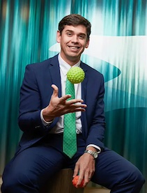 An Alumni in a blue suit and green tie tossing a toy ball.