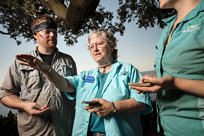 Three people standing. One is pointing in the distance to the left.