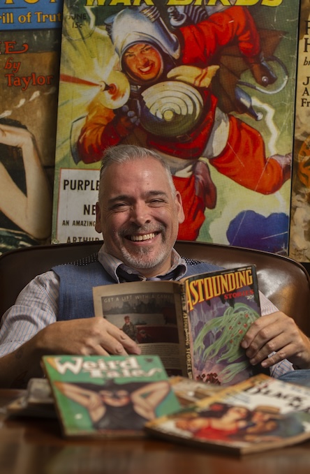 A man seated in front of art posters holding classic comic books.