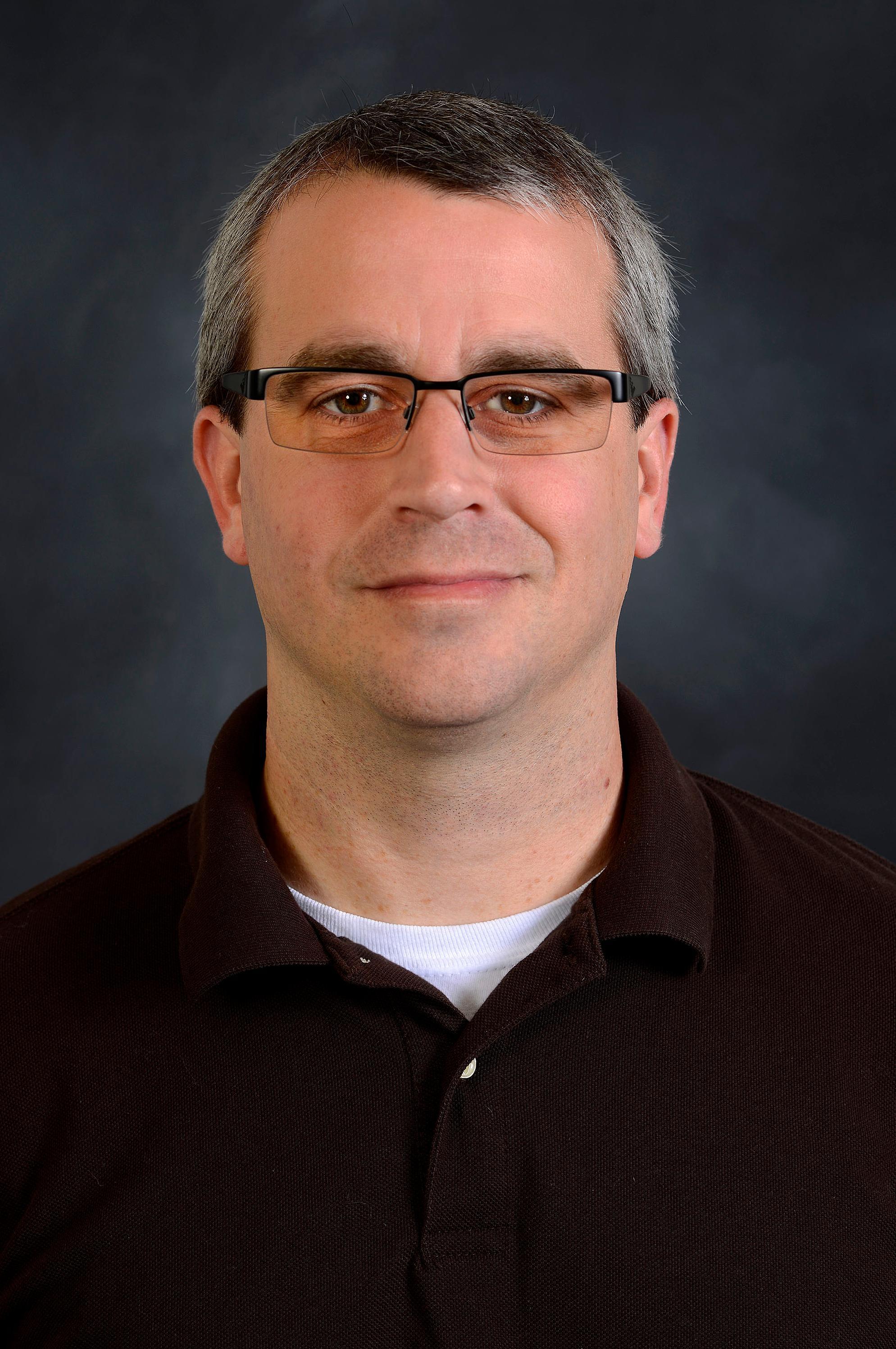 Jonathan Hovell indoor headshot in a black polo shirt against a dark gray background.