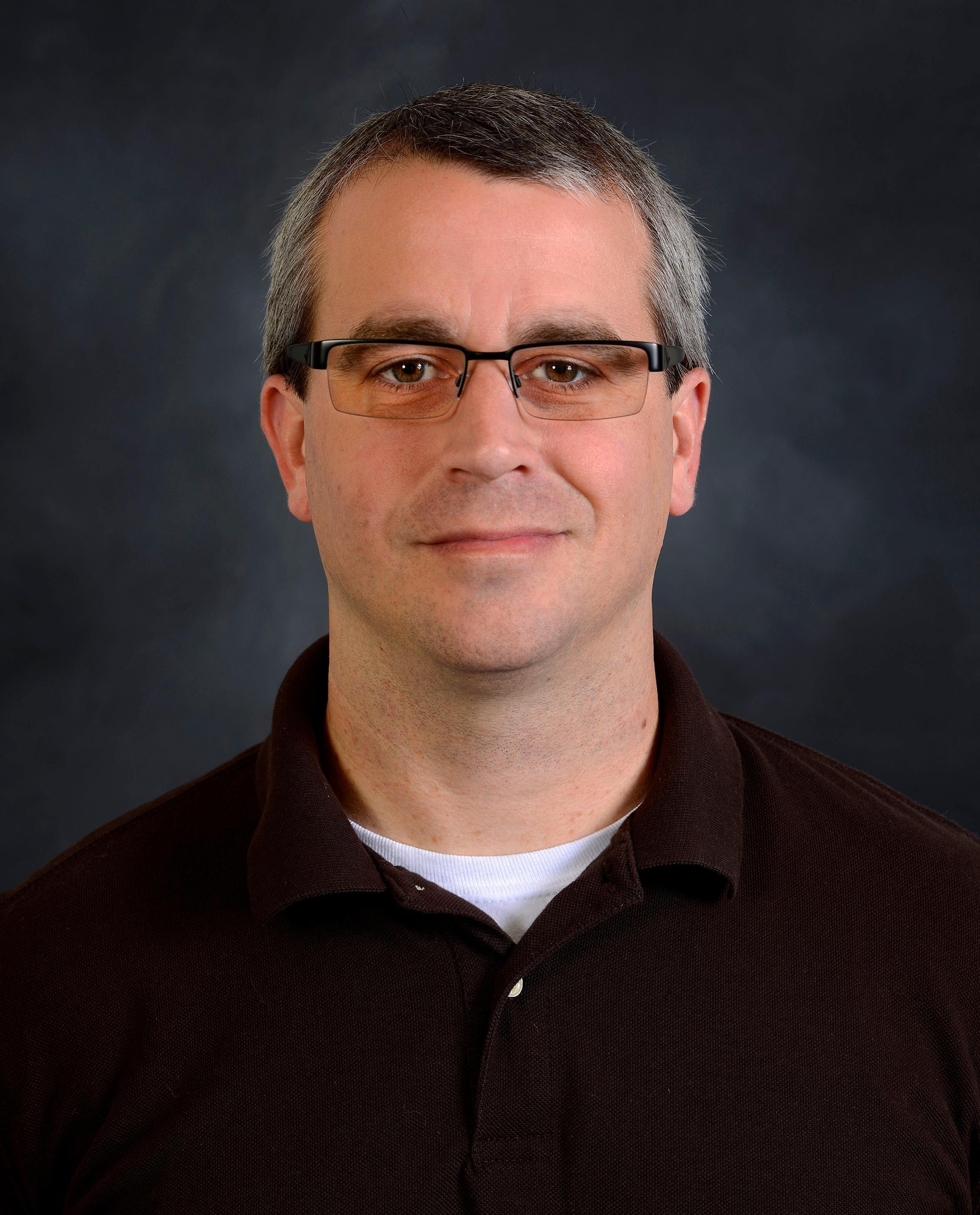 Jonathan Hovell indoor headshot in a black polo shirt against a dark gray background.