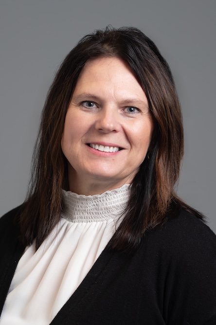 A staff member with a white shirt and black jacket and medium brown hair.