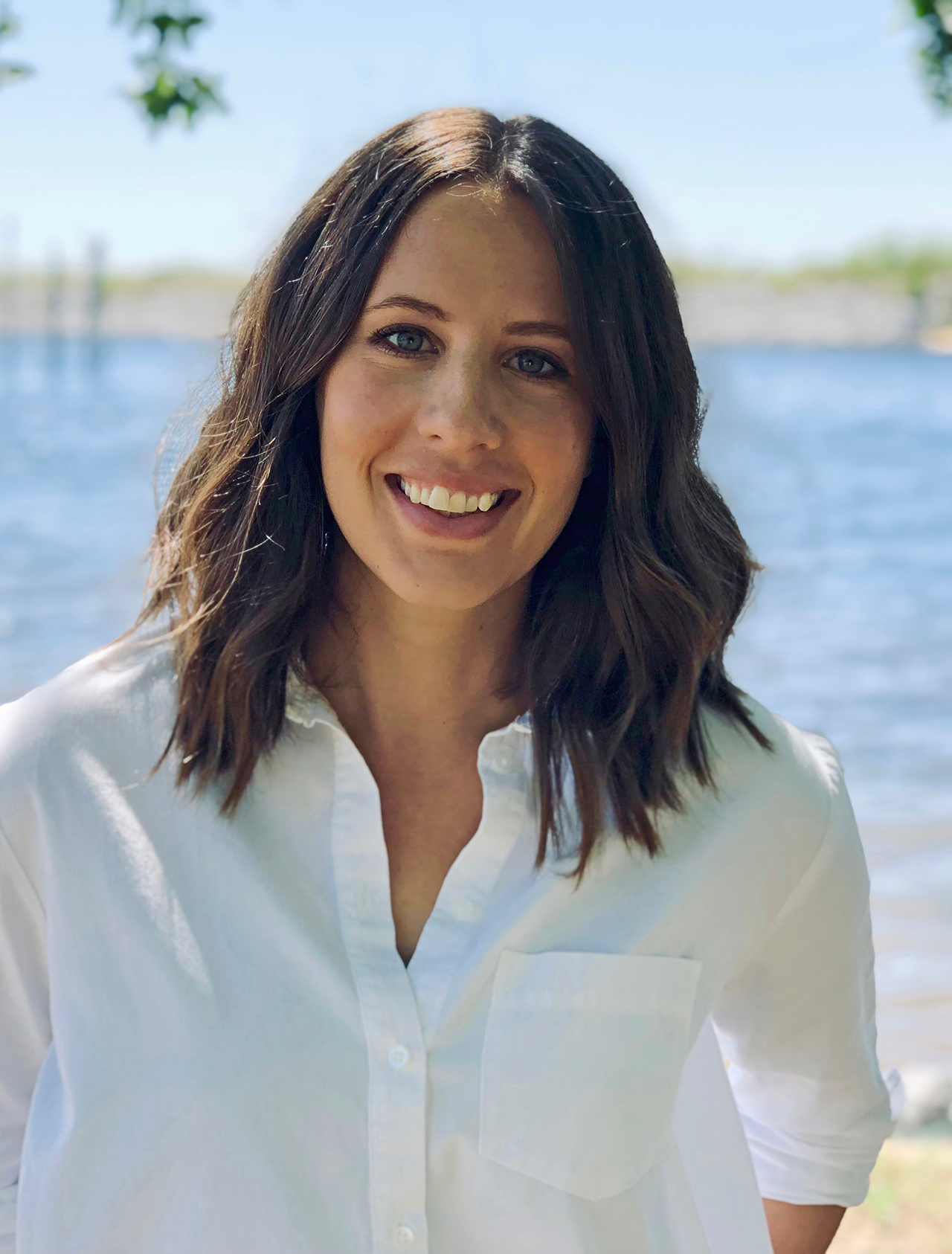 Nicole Grinnan in a white blouse standing in front of water and trees.