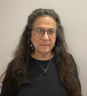 A headshot of a guest speaker with long brown hair wearing glasses and a black sweater.