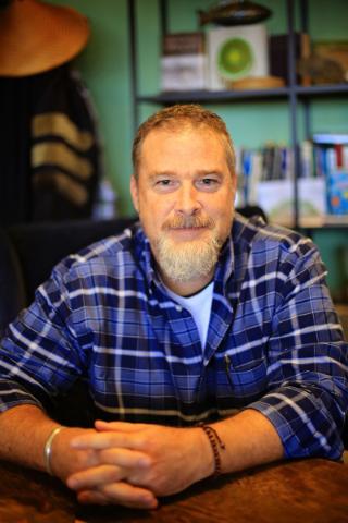 Man in blue plaid shirt sitting at desk.