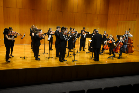 A group of musicians playing instruments around a conductor.