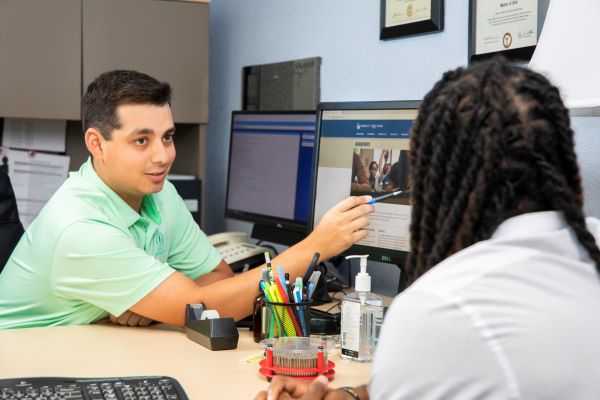 Admissions counsellor pointing to a laptop while talking with a student in an office setting
