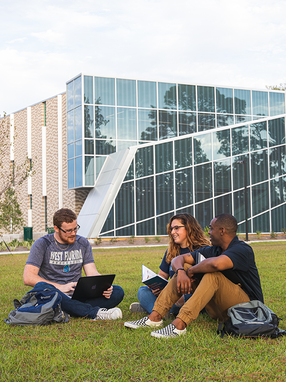 three students sitting on grass in front of building 58C