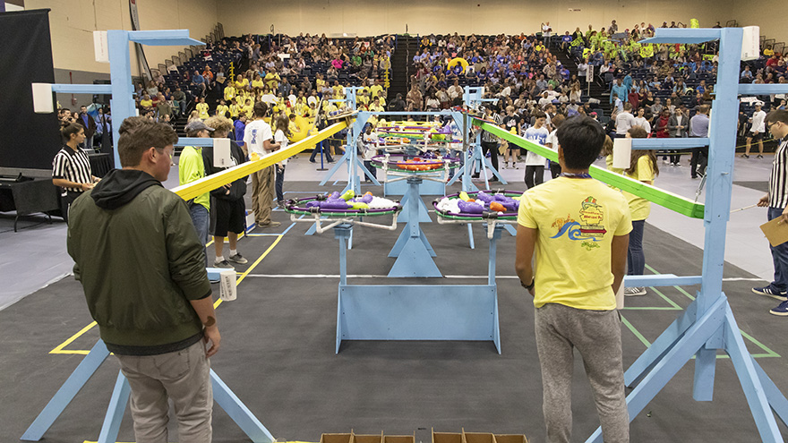 two robotics competitors facing their robots and the crowd in the background