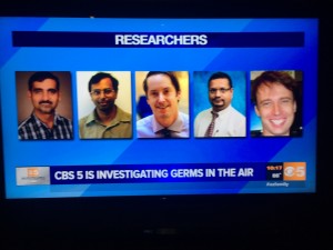 A TV broadcast showing headshots of five people labeled as researchers, with a CBS 5 news ticker about investigating germs in the air.