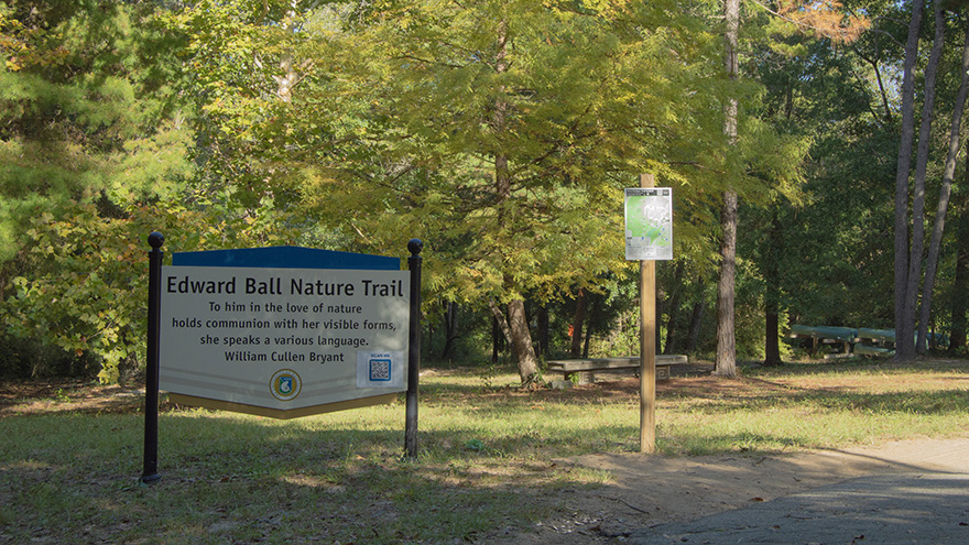 Edward Ball Nature Trail sign in front of trees and a couple of wooden benches.