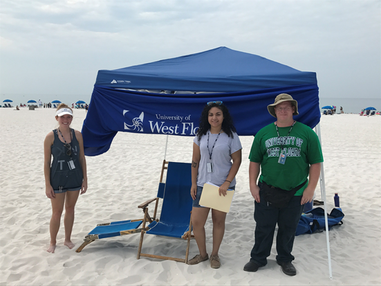 three students standing next to tent on beach