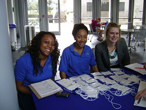 Three UWF Math Association members sitting an indoor clothed table with event name tags present on top of the table.