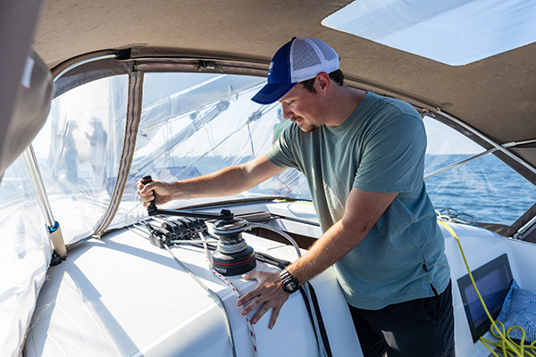 A person operating a winch in the cockpit of a sailboat traveling across the water.
