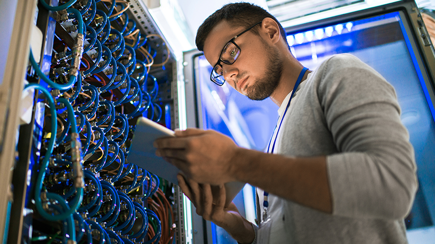 Male student in server room holding iPad