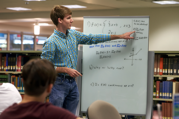 Student at whiteboard in library tutoring other students