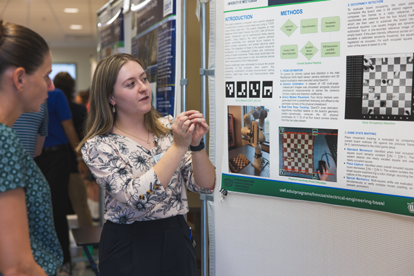 Student explaining their research to a professor in front of poster.