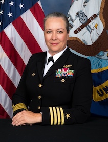 Woman dressed in military uniform with American flag in background.
