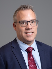 Headshot of man dressed in navy suit with a red tie