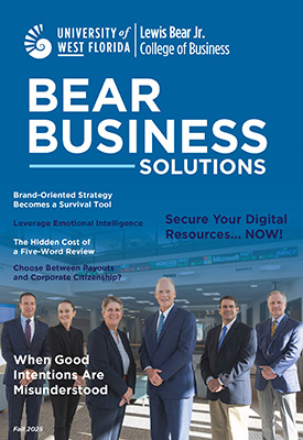 UWF Lewis Bear Jr. College of Business Bear Business Solutions Fall 2025 magazine cover showcasing six faculty in suits standing indoors in front of a rolling stock ticker.