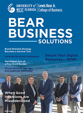 UWF Lewis Bear Jr. College of Business Bear Business Solutions Fall 2025 magazine cover showcasing six faculty in suits standing indoors in front of a rolling stock ticker.