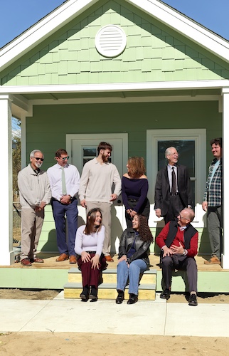 Three people sitting on steps and six people standing on porch of tiny home