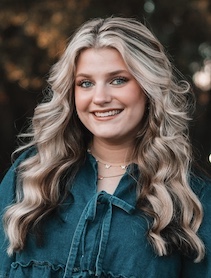 Headshot of woman with long curly blond hair, wearing a green shirt