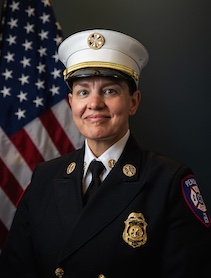Woman in police uniform including white police hat with American flag in background