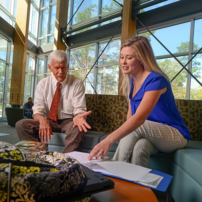 Professor advising a student while both are sitting on a lobby couch.