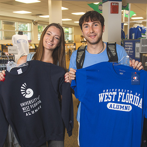 Two students holding University of West Florida alumni t-shirts in the UWF bookstore.