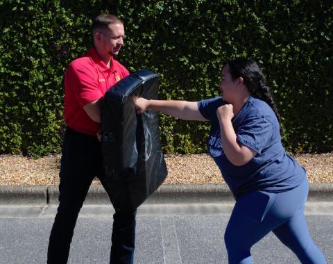 student punching a punching bag held by a UWF police officer, part of self defense training