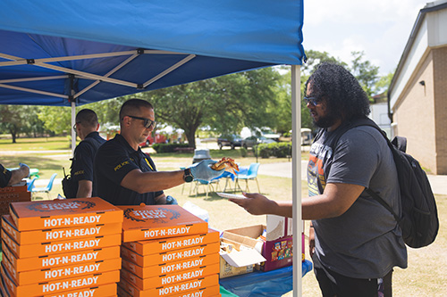 UWF Police Officer handing a piece of pizza to a student