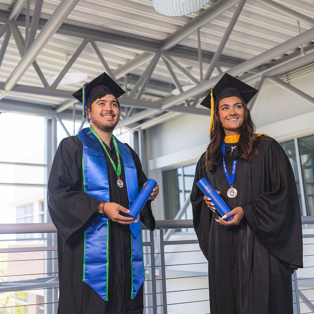 two uwf graduates holding diplomas