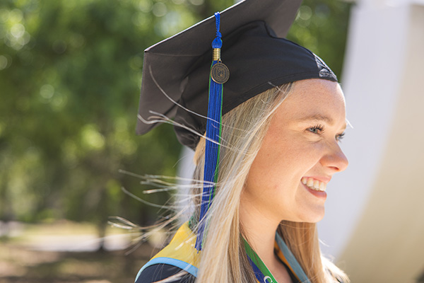 UWF student in cap and gown attire smiling.