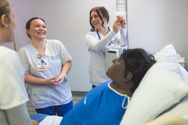 Nursing students smiling and attaching an IV to a simulation doll.