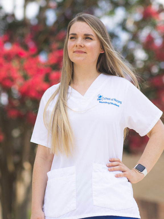 Nursing student stands in front of flowering tree on UWF campus